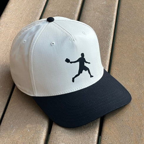 White and black cap with a black silhouette of a baseball player on a wooden surface